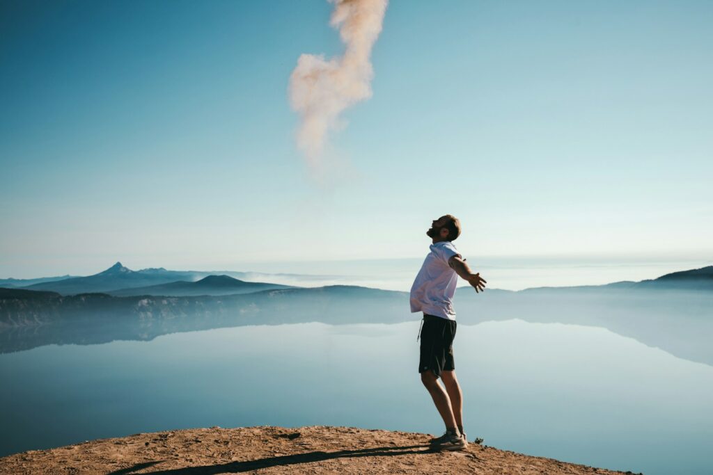 man standing on sand while spreading arms beside calm body of water