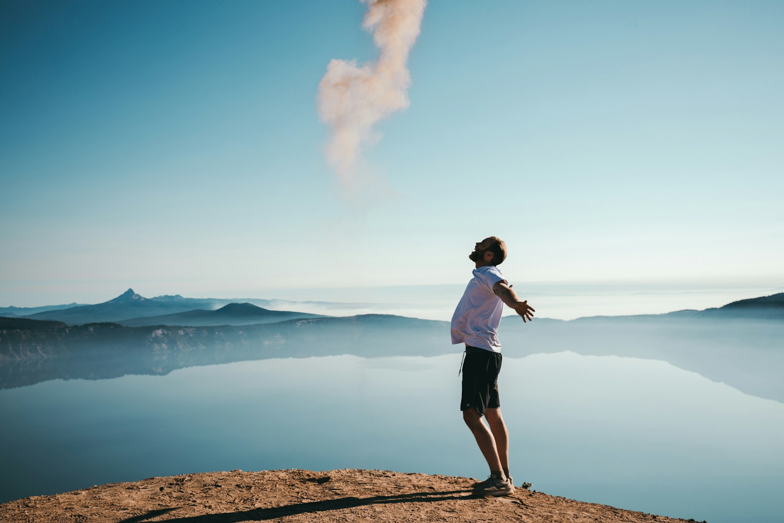 man standing on sand while spreading arms beside calm body of water