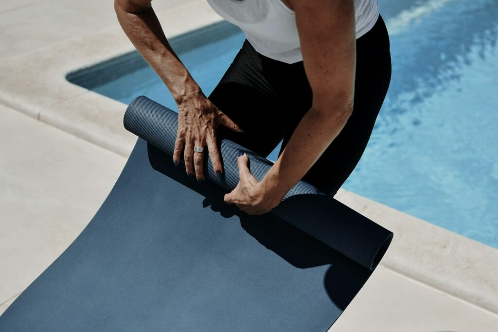 A man holding a yoga mat near a swimming pool